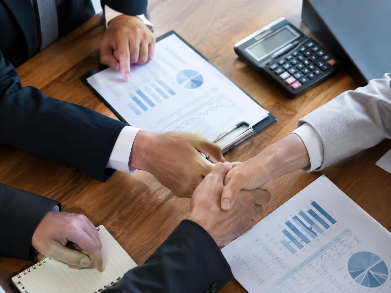 Financial disclosure documents and a calculator on a table as two people shake hands